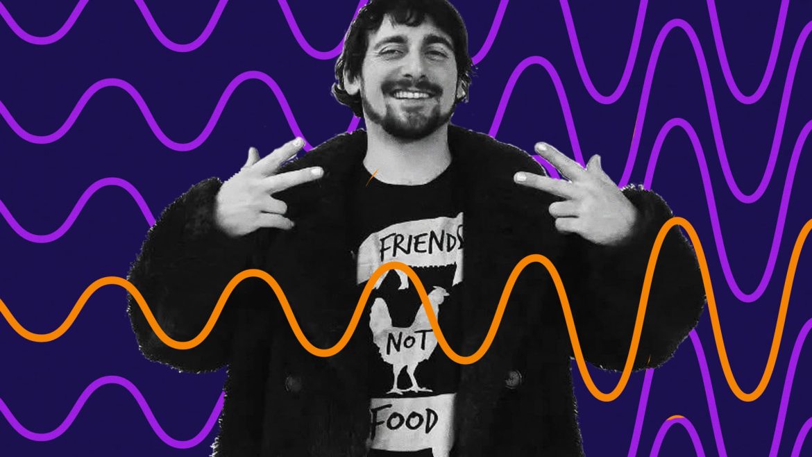 DJ Keano smiles and makes peace signs to the sides of his shoulders